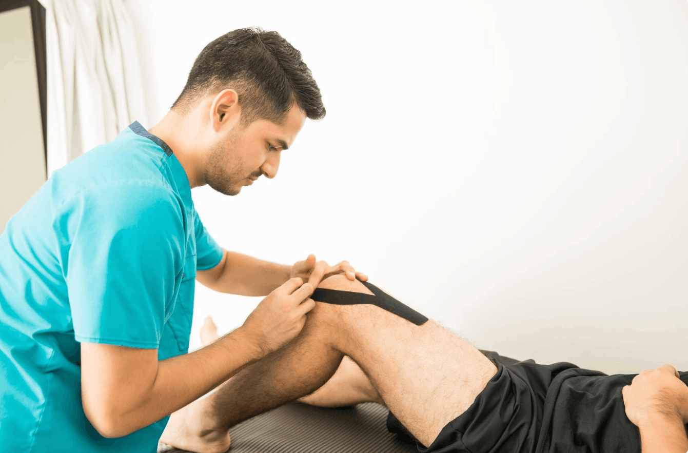 physiologist applying kinesiology tape on patient's knee